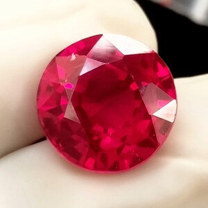 Peut inclure: Gros plan sur un rubis rond et facetté. La pierre précieuse rouge vif présente de nombreuses facettes qui captent la lumière. Le rubis est d'une couleur riche et saturée, sur fond blanc.