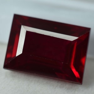 May include: A deep red rectangular gemstone with a faceted cut.