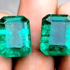 May include: Two emerald green gemstones, cut in a rectangular shape with beveled edges. The gemstones are faceted and have a translucent appearance.