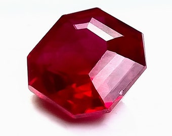Puede incluir: Una piedra preciosa de color rojo intenso con un corte facetado. La piedra preciosa tiene forma octogonal y un alto pulido.