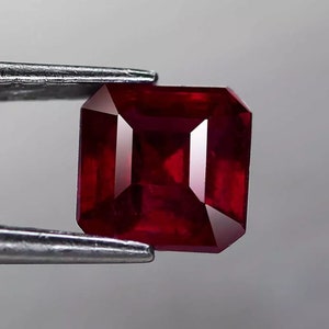 Puede incluir: Una piedra preciosa de forma cuadrada de color rojo intenso con un corte facetado.