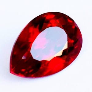 Peut inclure: Une pierre précieuse en forme de poire d'une couleur rouge profond et vibrante, dotée de multiples facettes créant une surface étincelante et réfléchissante. La pierre présente une pointe et une base arrondie avec une finition polie.