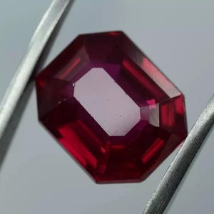 Peut inclure: Une pierre précieuse rouge foncé de taille rectangulaire octogonale. La pierre précieuse est tenue dans une pince.