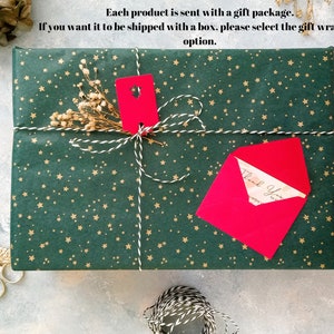 May include: A wrapped gift with green paper featuring gold stars, tied with white and gold twine. A red tag and envelope are attached. The text on the envelope reads "Thank You".