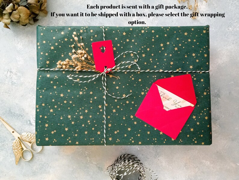 May include: A wrapped gift with green paper featuring gold stars, tied with white and gold twine. A red tag and envelope are attached. The text on the envelope reads "Thank You".
