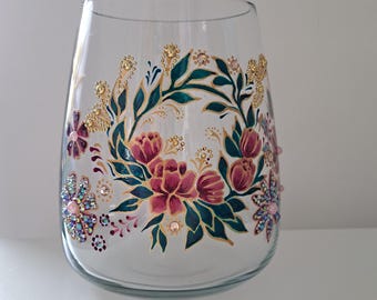 May include: A clear glass vase with a floral design. The vase features a painted wreath of pink and red flowers with green leaves and gold accents. Sparkling rhinestones are also applied to the vase, adding a touch of glamour.