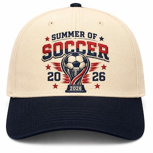 May include: A baseball cap with a cream-colored crown and a navy blue brim. The cap features the text "SUMMER OF SOCCER" in red and blue, along with a soccer ball graphic and the year "2026".