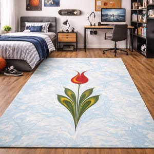 May include: A rectangular area rug with a light blue marbled background and a large floral design. The floral design features a red tulip with yellow accents and green leaves. The rug is placed on a hardwood floor in a bedroom.
