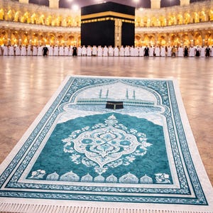 May include: A teal prayer rug with an ornate white floral design is laid out on a polished floor. The rug is in front of the Kaaba, a black cube-shaped building in Mecca, Saudi Arabia, with a crowd of people in white robes.