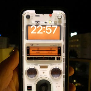 Puede incluir: Un smartphone con una funda transparente que muestra una interfaz de radio retro. La pantalla muestra la hora, "22:57", y la fecha, "Donnerstag, 28. März". El diseño incluye elementos naranjas y blancos, con texto en la parte inferior.