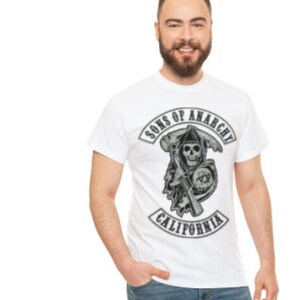 Peut inclure: T-shirt blanc avec un imprimé graphique noir et blanc d'un crâne portant un casque de moto avec le texte "Sons of Anarchy California".