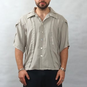 May include: A light grey short-sleeved button-down shirt with a collar. The shirt has a relaxed fit and a slightly textured fabric.