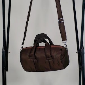 May include: A brown quilted duffel bag with a long adjustable strap. The bag has a zipper closure and two top handles.