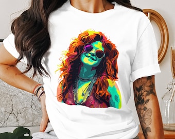 May include: White t-shirt featuring a vibrant pop art portrait of a woman with sunglasses and long, curly red hair. The artwork uses bright colors like yellow, green, and purple. The shirt is a classic crew neck style.