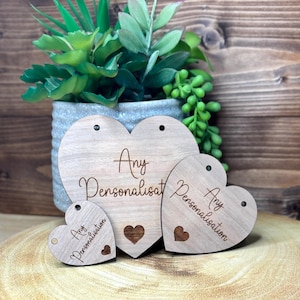 May include: Three wooden heart-shaped tags with the text "Any Personalisation" on each. The tags are different sizes and are arranged in a row on a wooden surface.