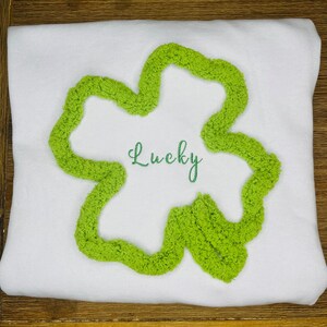 Op de afbeelding: Wit T-shirt met een groen klavertje vier design en het woord "Lucky" geborduurd.