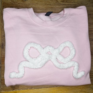 May include: A pink sweatshirt with a white fluffy bow design.