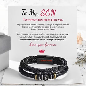 Pode incluir: Um bracelete de couro preto trançado com detalhes dourados. O bracelete tem um fecho que diz "Custom Name". O bracelete é acompanhado por um cartão com uma mensagem para um filho, que diz "To My SON Never forget how much I love you." O cartão também inclui uma mensagem sobre encontrar algo bom todos os dias, seguir os seus sonhos e lembrar-se de ser incrível.