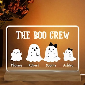 May include: A rectangular LED night light with a wooden base. The light features the text "THE BOO CREW" above four cartoon ghosts, each with a name below. The ghosts are white with black accents and bows.