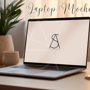 May include: A silver laptop computer with a blank screen displaying a logo for "sasuartistry". The laptop is on a wooden table with a lit candle, a cup, and a plant in a pot.