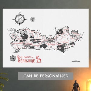 May include: A white map of the Royal County of Berkshire featuring black ink illustrations of forests and terrain, red text labels for towns like Reading and Newbury, a compass rose, a coat of arms, a deer icon, and a scale bar in miles.