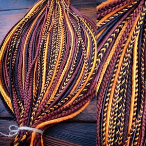 May include: A bundle of colorful dreadlocks in shades of brown, orange, and black. The dreadlocks are braided and tied together with twine. The color combination creates a striking visual effect, suitable for various hairstyles.