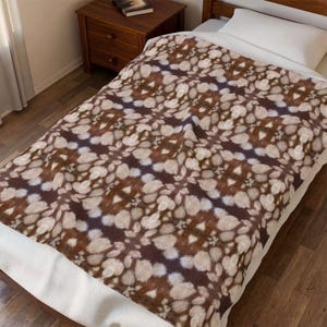 May include: A rectangular throw blanket featuring a repeating pattern of brown and cream-coloured fur-like textures. The design consists of dark brown patches interspersed with lighter, fluffy cream-coloured spots, creating a dense, organic appearance.