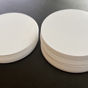 May include: Two stacks of white round paper circles. The stacks are different sizes. The circles are stacked on top of each other.