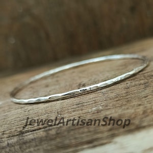 Könnte beinhalten: Ein silbernes Armreif-Armband mit gehämmertem Muster, präsentiert auf einer Holzoberfläche. Der Text "JewelArtisanShop" ist sichtbar. Der Durchmesser des Armbands beträgt ca. 6,5 cm.