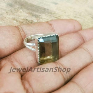 Könnte beinhalten: Ein silberner Ring mit einem großen, rechteckigen Rauchquarz-Edelstein. Der Edelstein hat eine durchscheinende braune Farbe mit einem facettierten Schliff. Der Ring hat ein schlichtes Band und eine dekorative Lünettenfassung. Der Text "JewelArtisanShop" ist sichtbar.