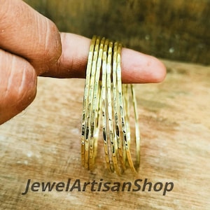Könnte beinhalten: Ein Satz goldfarbener Armreifen mit gehämmerten Texturen. Die Armreifen sind gestapelt, und das Bild ist aus der Nähe aufgenommen. Der Text "JewelArtisanShop" ist unten im Bild zu sehen.