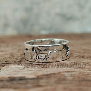 May include: A silver ring with a horse design. The ring is made of a shiny metal and features a continuous band with cut-out horse silhouettes. The ring is displayed on a wooden surface.