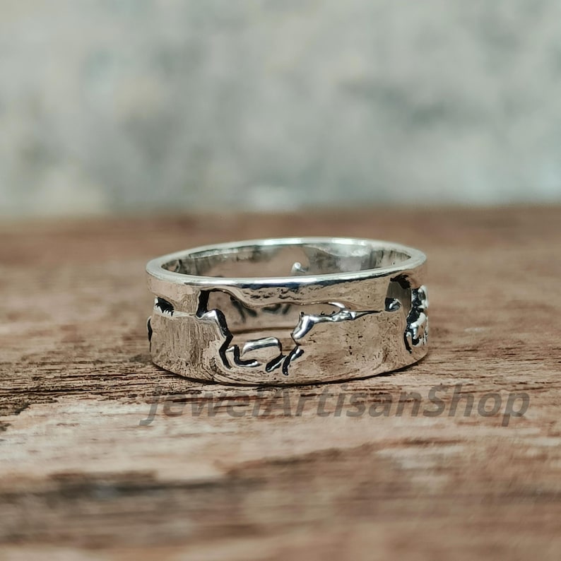 May include: A silver ring with a horse design. The ring is made of a shiny metal and features a continuous band with cut-out horse silhouettes. The ring is displayed on a wooden surface.
