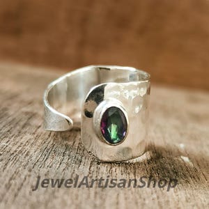 Könnte beinhalten: Silberfarbener Ring mit gehämmertem Muster und einem ovalen, mehrfarbigen Edelstein. Der Ring hat ein offenes Design. Der Text "JewelArtisanShop" ist unten sichtbar.