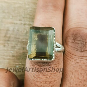 Könnte beinhalten: Silberring mit einem großen, rechteckigen, olivgrünen Edelstein. Der Edelstein ist in einer Silberfassung gefasst. Der Ring befindet sich an einem Finger. Der Text "JewelArtisanShop" befindet sich unten.