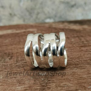 May include: A silver-colored ring with a unique, open design. The ring features a series of curved, connected bands, creating a spiral effect. The polished metal reflects light, highlighting the ring's intricate form. The ring is a piece of jewelry.