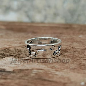 May include: A silver ring featuring a continuous horse design. The ring is set against a wooden surface. The ring's design features cut-out silhouettes of horses around the band. The ring is a piece of jewellery.