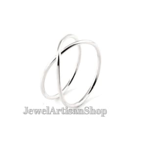 Könnte beinhalten: Ein silberfarbener Ring mit minimalistischem Design. Der Ring hat zwei ineinander verschlungene Bänder, die sich kreuzen. Der Ring ist vor einem weißen Hintergrund platziert. Der Text "JewelArtisanShop" befindet sich unten.