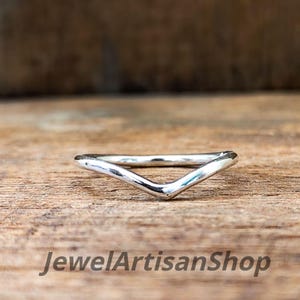 Könnte beinhalten: Ein silberner, V-förmiger Ring. Der Ring befindet sich vor einem hölzernen Hintergrund. Der Text "JewelArtisanShop" ist unten im Bild zu sehen.