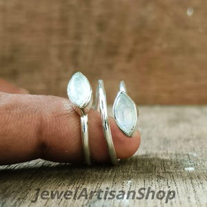 Könnte beinhalten: Ein silberner Ring mit Spiraldesign, der zwei tropfenförmige, hellfarbige Edelsteine aufweist. Der Ring ist um einen Finger gewickelt und zeigt das Design des Schmucks. Der Text "Jewel Artisan Shop" ist unten sichtbar.