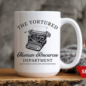 K&ouml;nnte beinhalten: Eine wei&szlig;e Keramiktasse mit einer Schwarzwei&szlig;illustration einer alten Schreibmaschine. Der Text auf der Tasse lautet "The Tortured Human Resources Department All's Fair in Love and Documenting".
