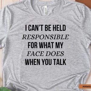 May include: Gray t-shirt with the text "I can't be held responsible for what my face does when you talk" printed on it.