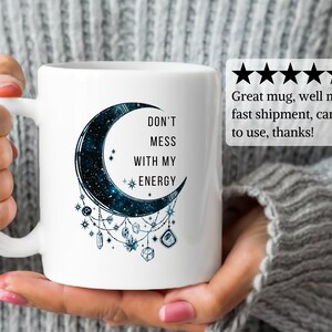 May include: White ceramic mug with a black crescent moon design. The moon has a galaxy pattern and is surrounded by crystals and stars. The text "DON'T MESS WITH MY ENERGY" is printed on the mug.