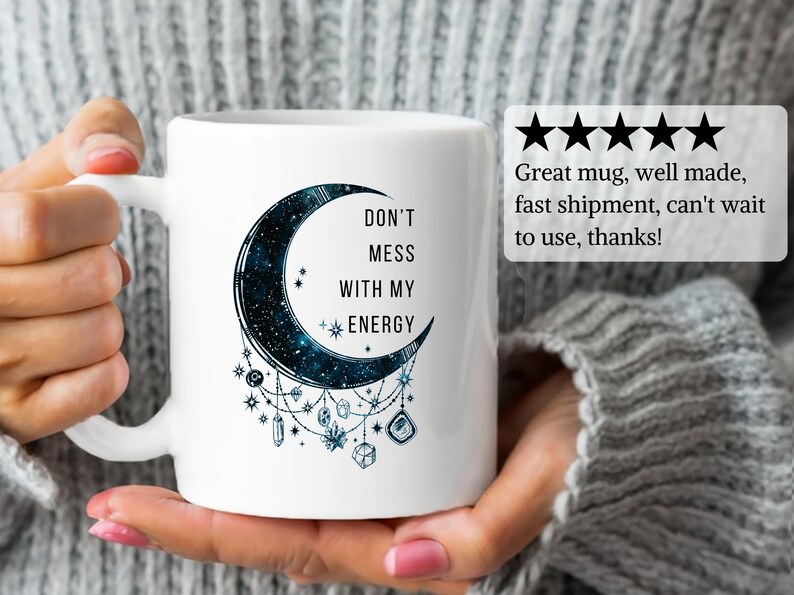 May include: White ceramic mug with a black crescent moon design. The moon has a galaxy pattern and is surrounded by crystals and stars. The text "DON'T MESS WITH MY ENERGY" is printed on the mug.