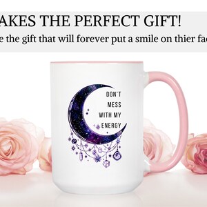 May include: White ceramic mug with a pink rim and handle. The mug features a crescent moon with a galaxy design and the text "Don't mess with my energy".