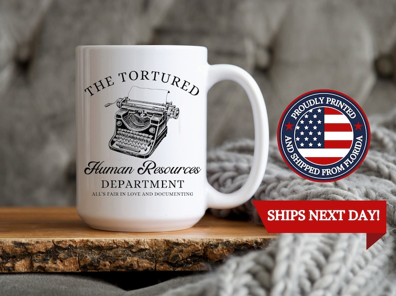 K&ouml;nnte beinhalten: Eine wei&szlig;e Keramiktasse mit einer Schwarzwei&szlig;illustration einer alten Schreibmaschine. Der Text auf der Tasse lautet "The Tortured Human Resources Department All's Fair in Love and Documenting".