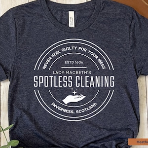 May include: Heather navy blue t-shirt with a white circle graphic that says "Never feel guilty for your mess. Est. 1606 Lady Macbeth's Spotless Cleaning Inverness, Scotland"