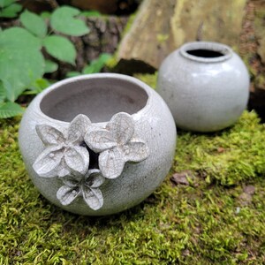 Peut inclure: Deux pots en céramique blanche avec un glaçage craquelé. Un pot a un motif floral en relief.