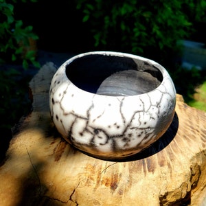 May include: A white ceramic bowl with a black crackle glaze. The bowl is sitting on a piece of wood.