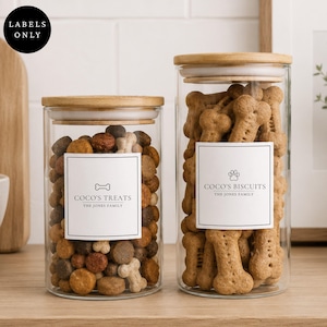 May include: Two clear glass cylindrical storage jars with light wood lids. The smaller jar is filled with round brown treats and labelled COCO'S TREATS THE JONES FAMILY. The taller jar contains bone-shaped biscuits and is labelled COCO'S BISCUITS THE JONES FAMILY.